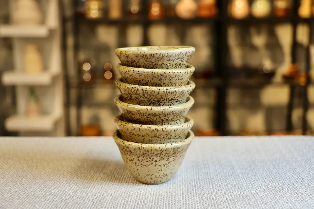 Six handleless Arabic coffee cups in a speckled glaze, stacked.