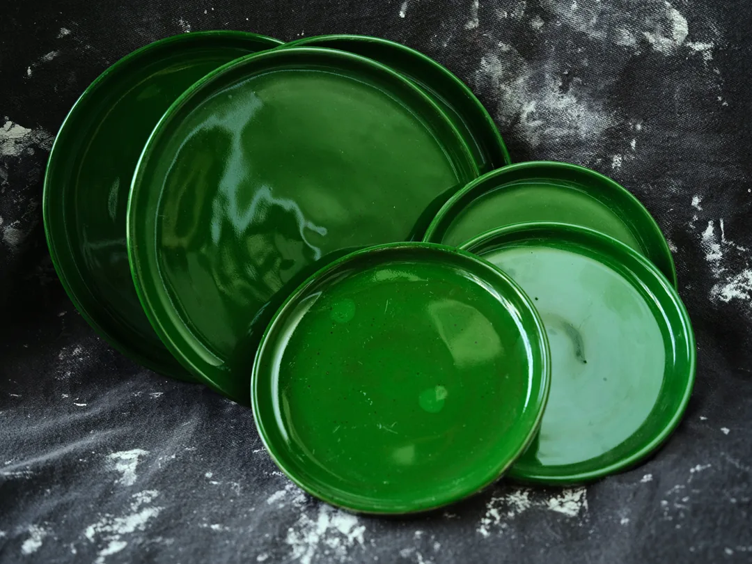 Glossy deep-green handmade plates in two sizes fanned out on a dark cloth.